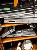 Stack of six DVD players on shelf showing front panels and brand markings