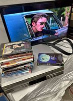 TV displaying video, combo player beneath, cabling visible, media stack showing titles