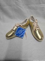 pair of metallic gold lace-up shoes with hang tag visible