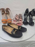 Group shot of four pairs: black loafers, orange heels, pink sandals, black rhinestone heels