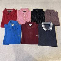All seven polo shirts laid flat, showing colors and brands