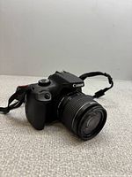 Front three-quarter view of Canon EOS Rebel camera with 18-55mm lens attached, strap visible