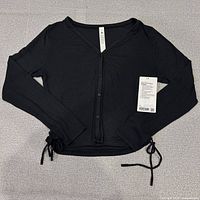 Front view of black ribbed cardigan with side ties and tags attached