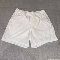 Front view of white Lululemon Pace Breaker shorts laid flat showing waistband, side pockets, perforated fabric