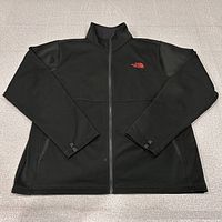 Front view of black North Face softshell jacket laid flat