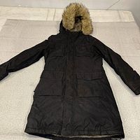 Full view of black TNA parka laid flat showing hood and length