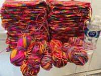 Stacks of hand-knitted squares with six yarn balls and water bottle for scale