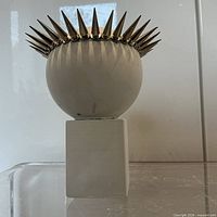 front view of spherical white head with metal spike crown on square pedestal