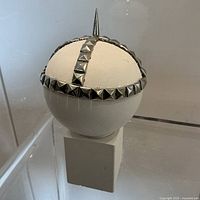 Frontal view of spherical head sculpture with studded metal bands and spike