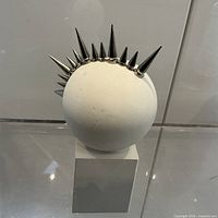 Front view of spherical white head on plinth with metal spikes