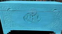 Front view of closed turquoise carved camphor wood trunk showing brass lock plate and carved panels
