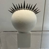 Front view of spherical head sculpture with metal spike crown on plinth