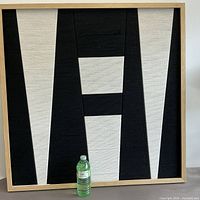 Full view of framed textile wall art with bottle for scale