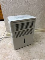 Front view of dehumidifier showing louvered intake and water-level window