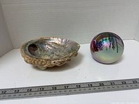 Abalone shell dish beside iridescent glass paperweight with ruler for scale