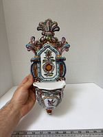Front view of ceramic holy water font held by hand showing full design