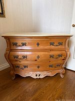 Front view showing bombe shape, drawers, hardware, carved base