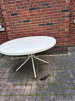 Oblique view of the entire round white patio table showing metal legs and surrounding area