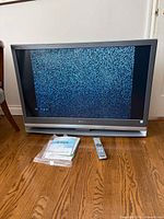 Front view of Sony 42in Grand Wega TV powered on showing static with accessories on floor