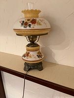 Front view of the vintage floral hurricane lamp showing glass shade, base, and metal foot