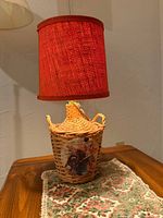 Full view of wicker bottle lamp with red shade on table