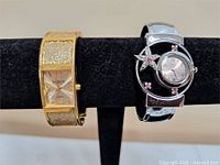 Joan Rivers gold-tone glitter cuff watch beside SAS silver-tone rhinestone cuff watch on display bar