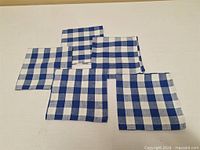 Five folded blue and white gingham napkins on flat surface