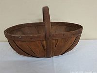 Side view of oval wooden basket showing handle and slat construction