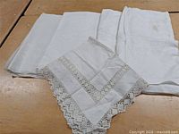 Four folded white linens on tabletop showing crochet-trimmed piece in foreground and three damask cloths behind