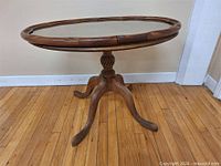 Full view of oval wood coffee table with glass insert and pedestal base