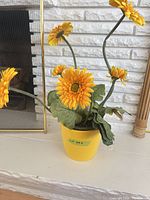 Full view of artificial yellow gerbera daisies in yellow pot on mantel