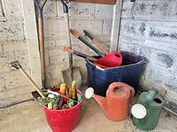 Group of long-handled tools, watering cans, buckets and tub