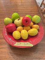 Red bowl filled with assorted artificial fruit placed on wooden table