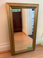 Full view of rectangular mirror with gold wood frame leaning against wall