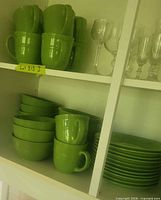 Green mugs, bowls and plates stacked in cabinet; shows colour, form and quantity