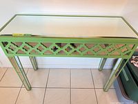 Front angled view of bright green console table showing mirrored glass top and quatrefoil apron