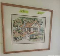 Full view of framed needlepoint cottage scene showing frame, mat and dimensions tag