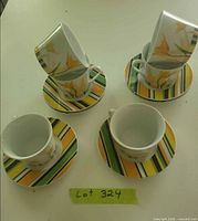 Four cup and saucer sets displayed on tabletop beside lot number