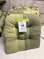 Stack of four green tufted cushions with auction lot tag