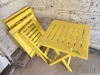 Open yellow folding table and three folded matching tables leaning against wall