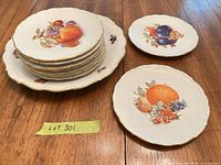 Stack of fruit motif plates and two single plates showing patterns and gold rims