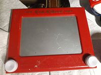 Front view of red Etch A Sketch showing screen and knobs