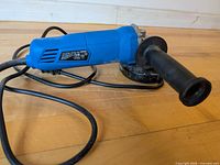 Angle grinder side view showing blue housing, cord and auxiliary handle