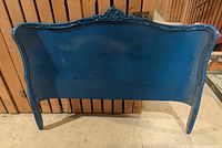 Front view of wooden headboard painted blue with carved crest