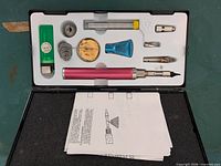 Open case showing soldering iron handle, tips, attachments, consumables, stand, refill container and instructions