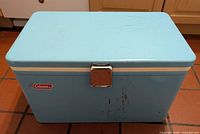 Front view of light blue Coleman metal cooler with chrome latch and logo