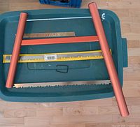 Disassembled anodized aluminum bow saw with main blade and packaged spare blade on bin lid