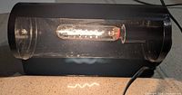 Front view of black wall lamp lit, showing bulb and housing