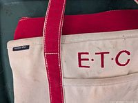 Front of tote showing brand tag, monogram, pocket, handle stitching
