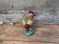 Full view of glazed ceramic rooster statue standing on green base